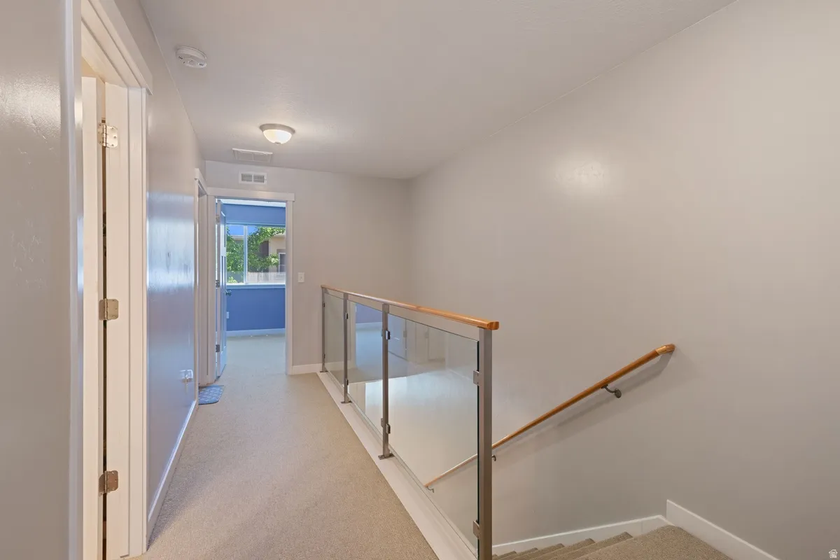 Upper level hallway with carpeted flooring, glass panel railing with wood-finish top rail, and recessed lighting
