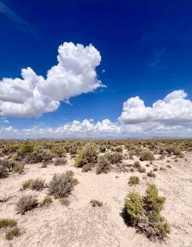Expansive open land featuring natural desert vegetation and a bright blue sky with scattered clouds