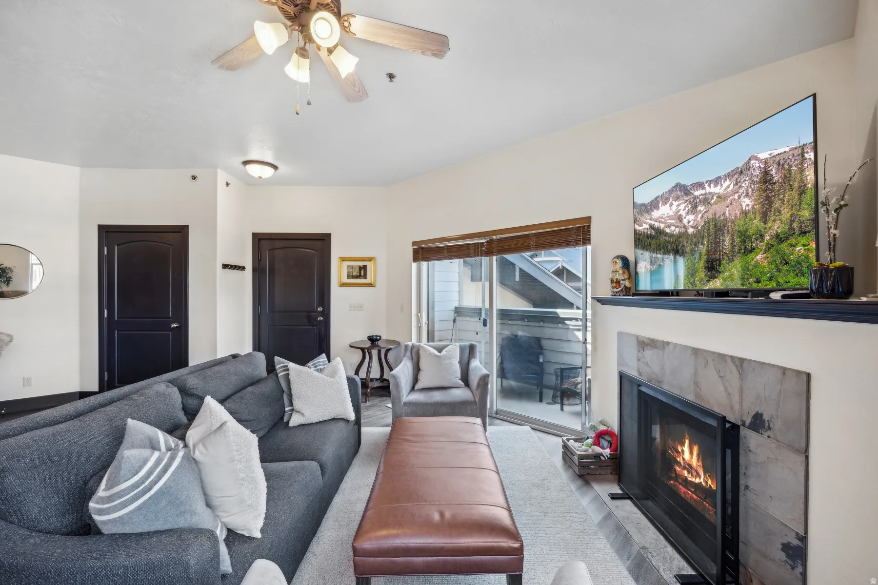 Living room featuring a fireplace with stone surround, ceiling fan, and sliding glass door to a private balcony