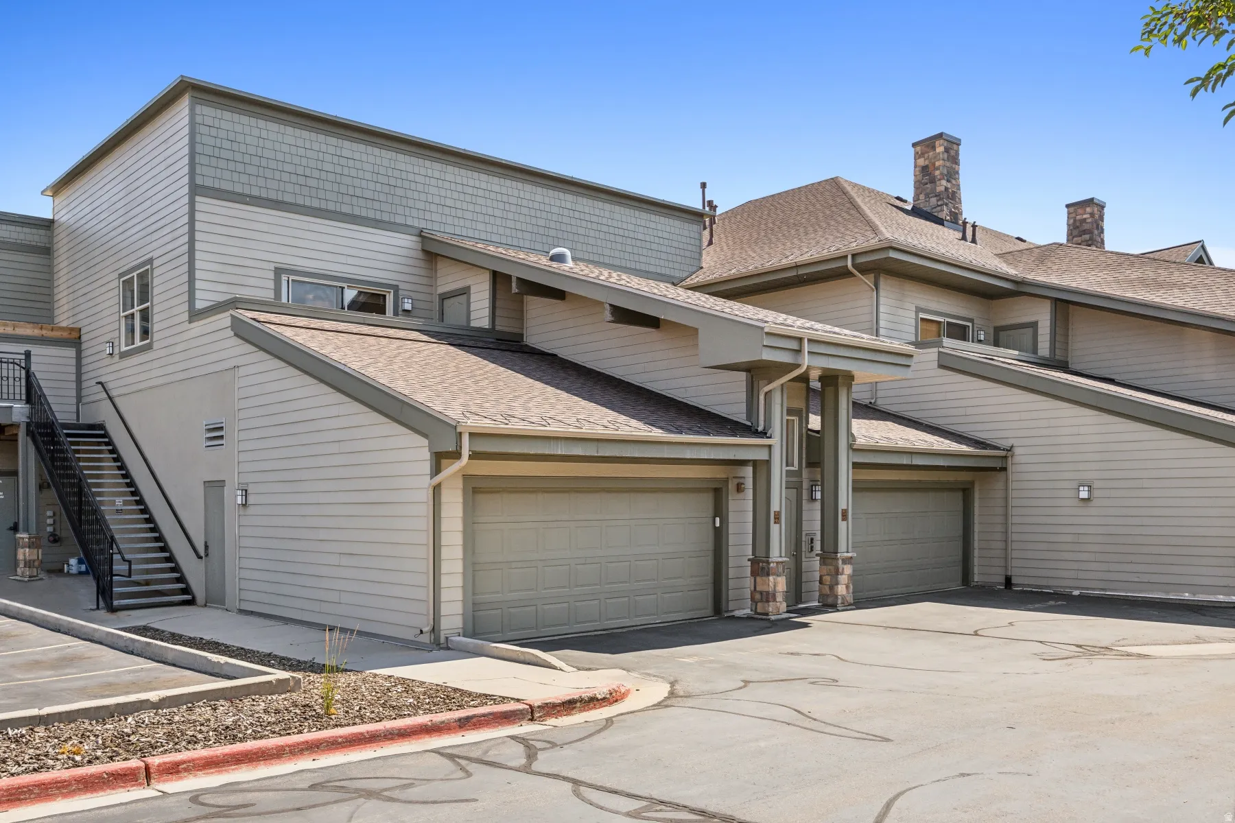 Exterior featuring horizontal siding, multiple attached garage bays, a prominent exterior staircase with metal railings, and stone-clad chimney details