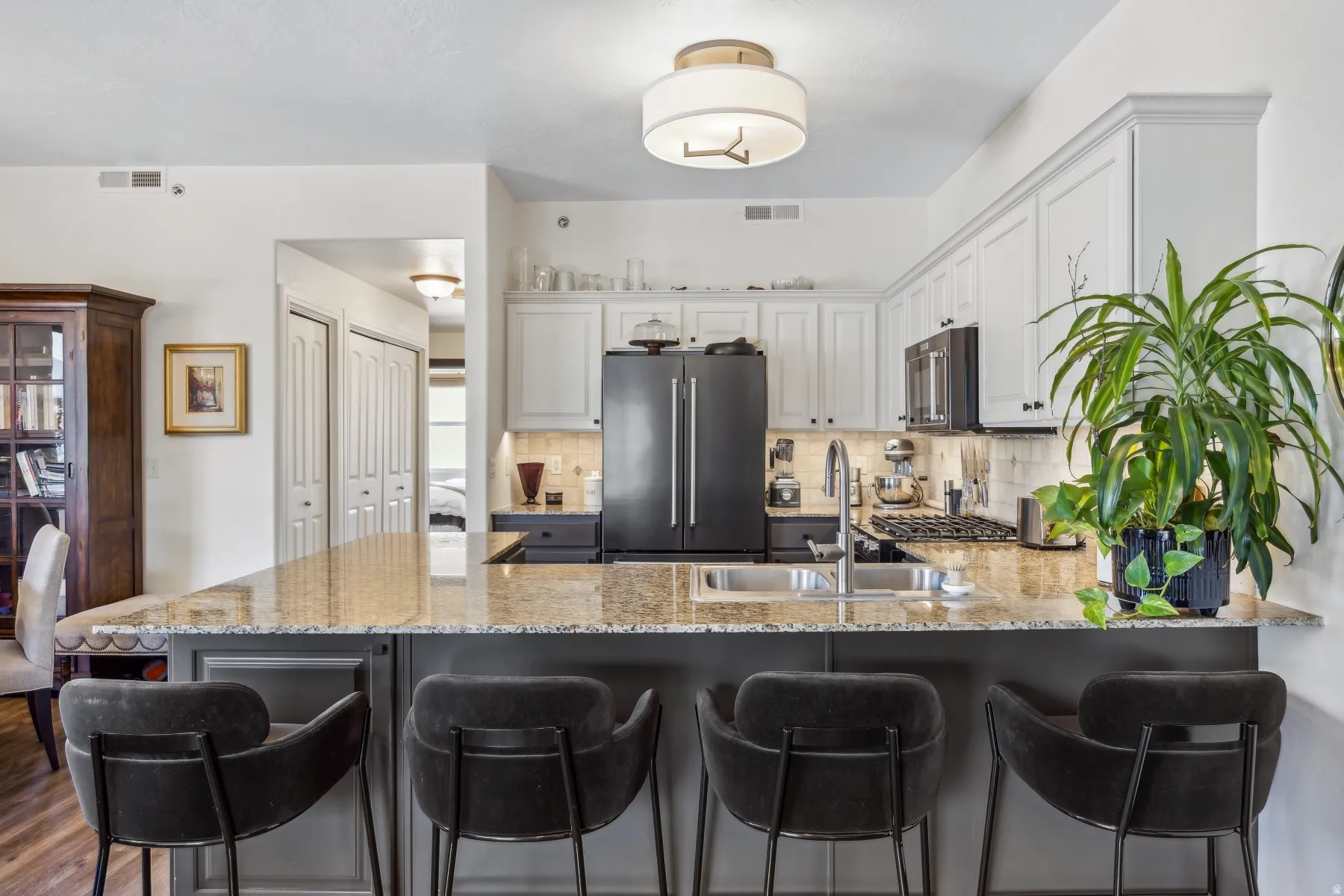 Kitchen featuring a large central island with seating, granite countertops, white upper cabinetry, dark lower cabinetry, and black appliances