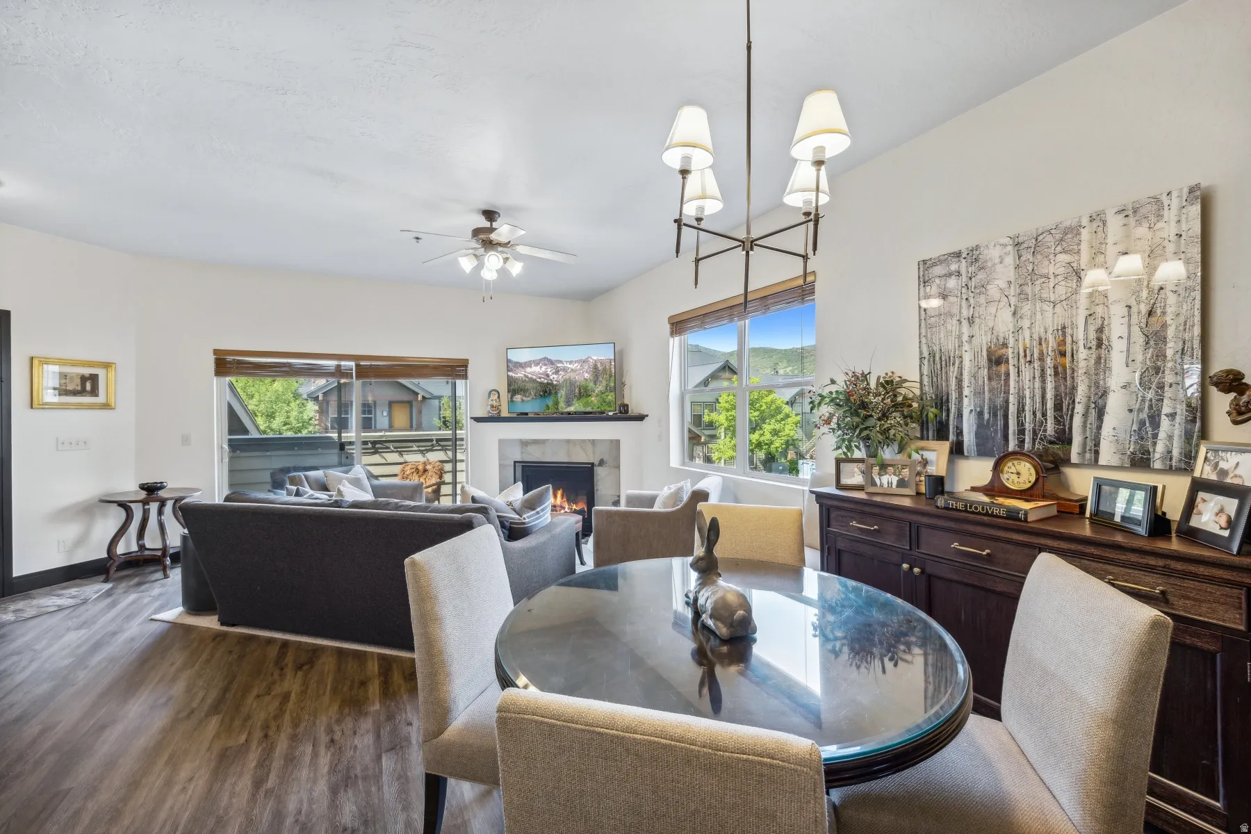 Open-concept living area with wood-finish flooring, a fireplace featuring a stone surround and mantel, and a dining area with a contemporary chandelier