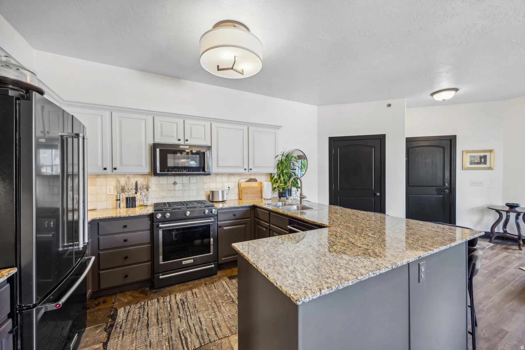 Kitchen featuring an expansive island with a light-colored countertop, two-toned cabinetry with gray upper cabinets and dark lower cabinets, a built-in microwave, a gas range, and a black refrigerator
