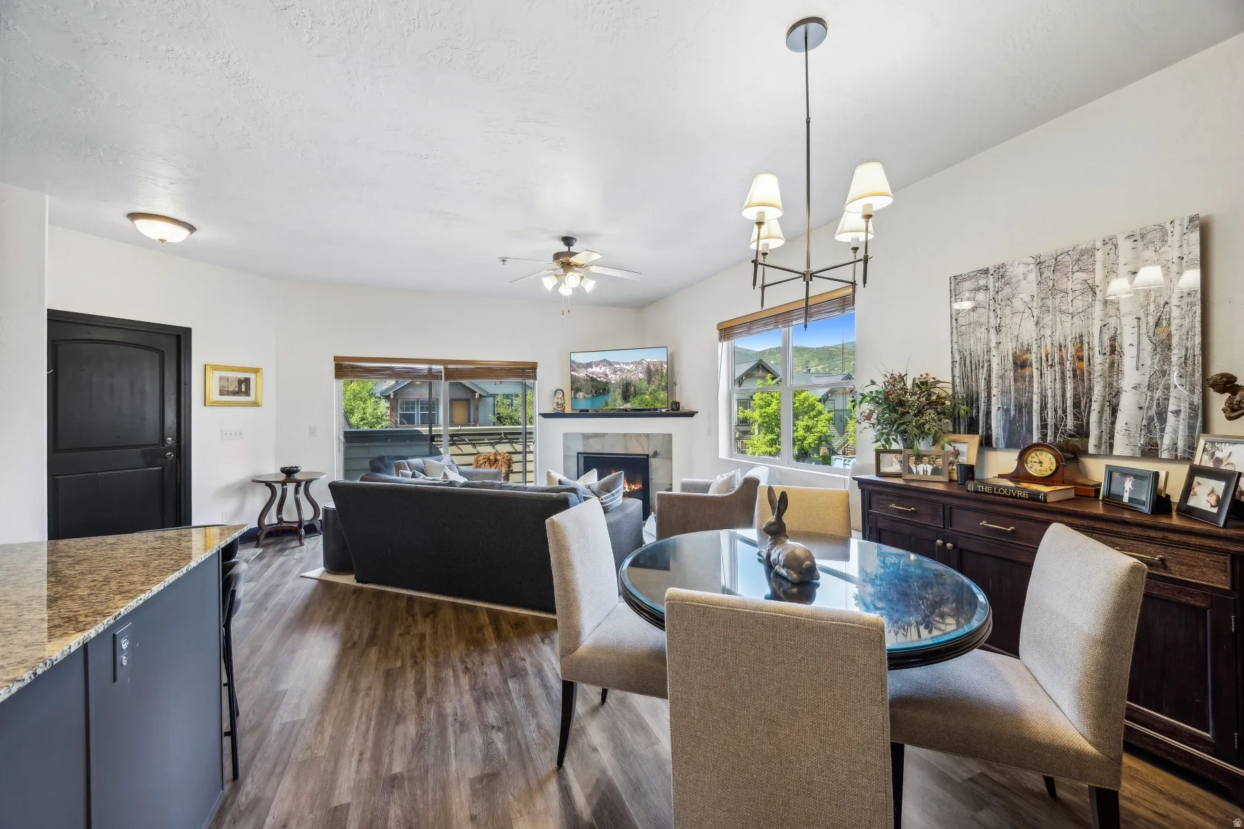 Open-concept living space featuring wood-finish flooring, a fireplace with a stone surround, and an integrated dining area with a modern chandelier