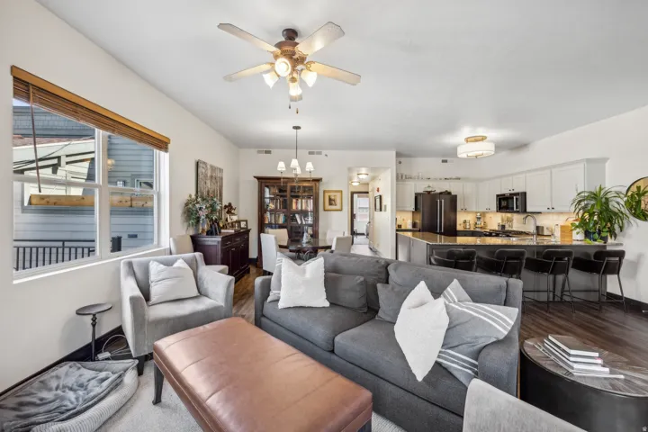 Open-concept living space featuring wood-finish flooring, a contemporary kitchen island with seating, white cabinetry, a built-in ceiling fan, and recessed lighting