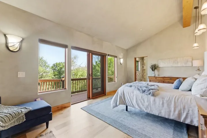 Vaulted ceiling room featuring light wood-finish flooring, a sliding glass door opening to an outdoor deck with wood railings, and two wall-mounted sconces
