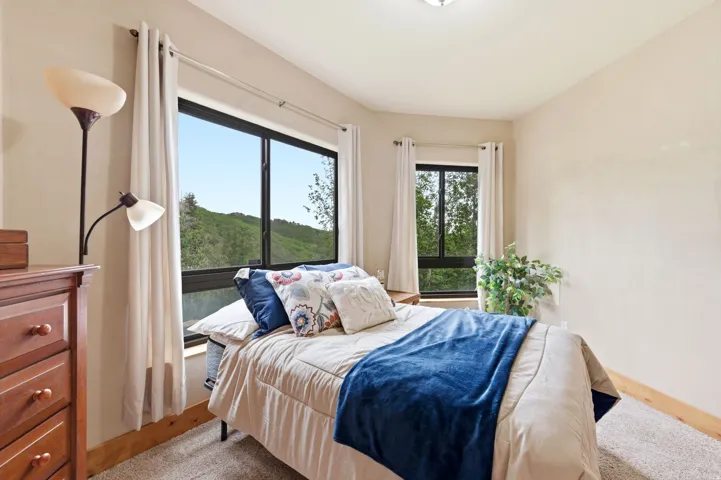Neutral-toned walls and carpeted flooring define this room, featuring multiple windows with black frames and light-colored drapes
