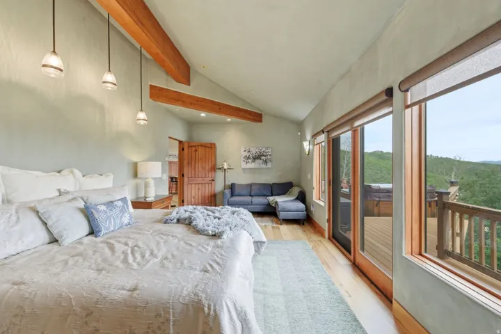 Spacious room featuring exposed wood beams, wood-finish flooring, a vaulted ceiling, and sliding glass doors opening to an exterior deck with a hot tub