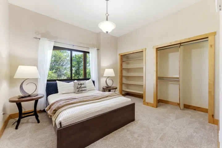 Carpeted room featuring a large window, a ceiling-mounted light fixture, and two closet openings