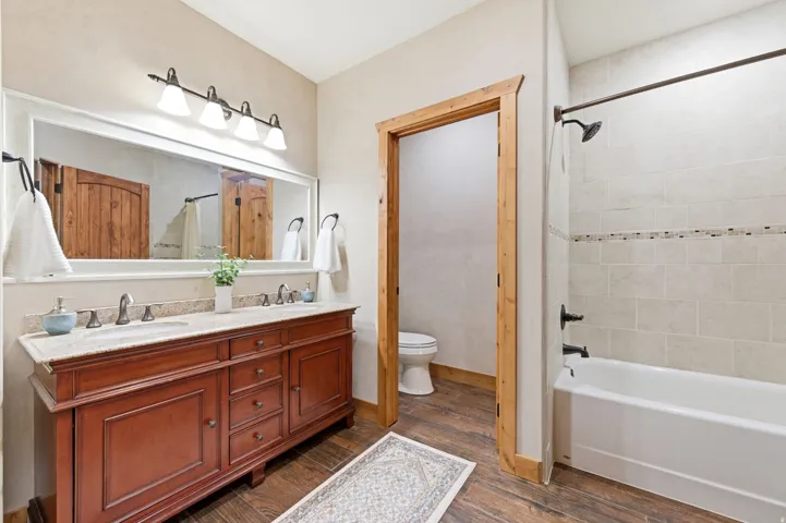 Bathroom featuring a dual-sink vanity with a light-toned countertop, a large mirror, and a built-in shower-over-tub combination with tiled surround