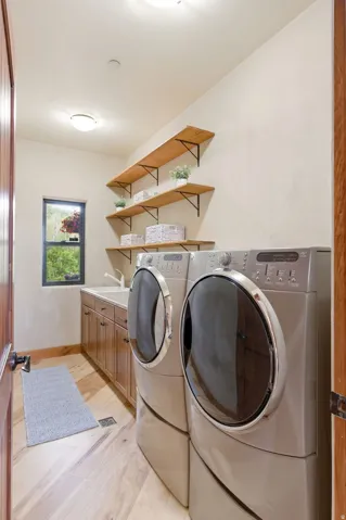 Laundry space featuring wood-finish flooring, built-in cabinetry with a countertop and sink, and open shelving