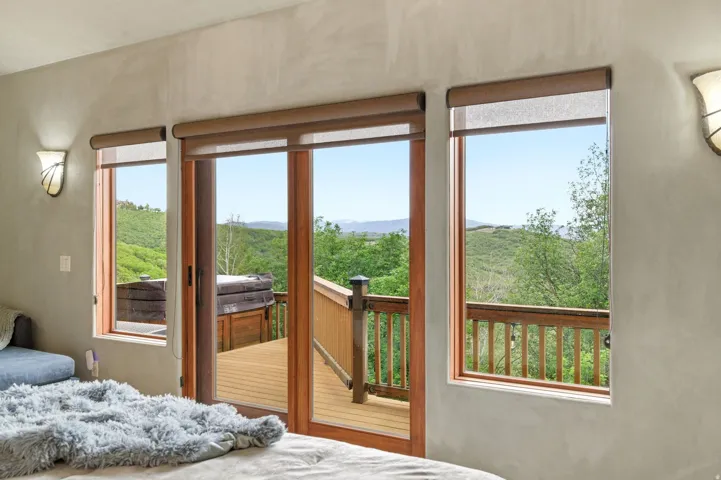 Room featuring three windows with neutral roller shades, a central sliding glass door, and two wall-mounted sconces with frosted glass