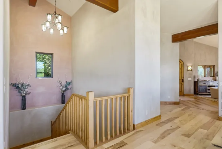 Vaulted ceilings featuring exposed wood beams and a multi-light chandelier
