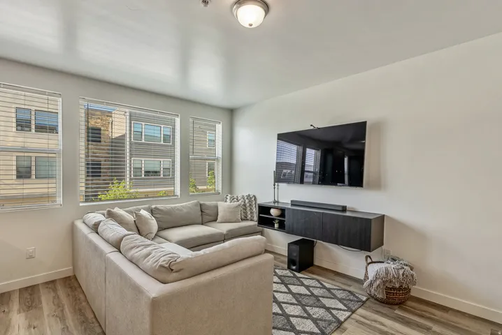 Living area featuring wood-finish flooring, multiple windows with blinds, a wall-mounted floating media console, and a contemporary ceiling light fixture