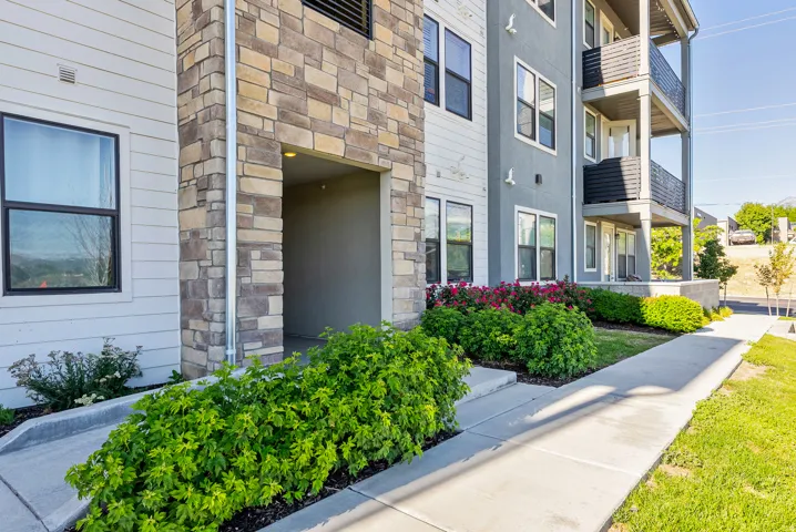 Exterior facade featuring stacked stone accents, horizontal siding, multiple balconies with metal railings, and ground-level landscaping