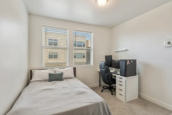 Bright room featuring two windows with blinds, light gray carpet, and white walls