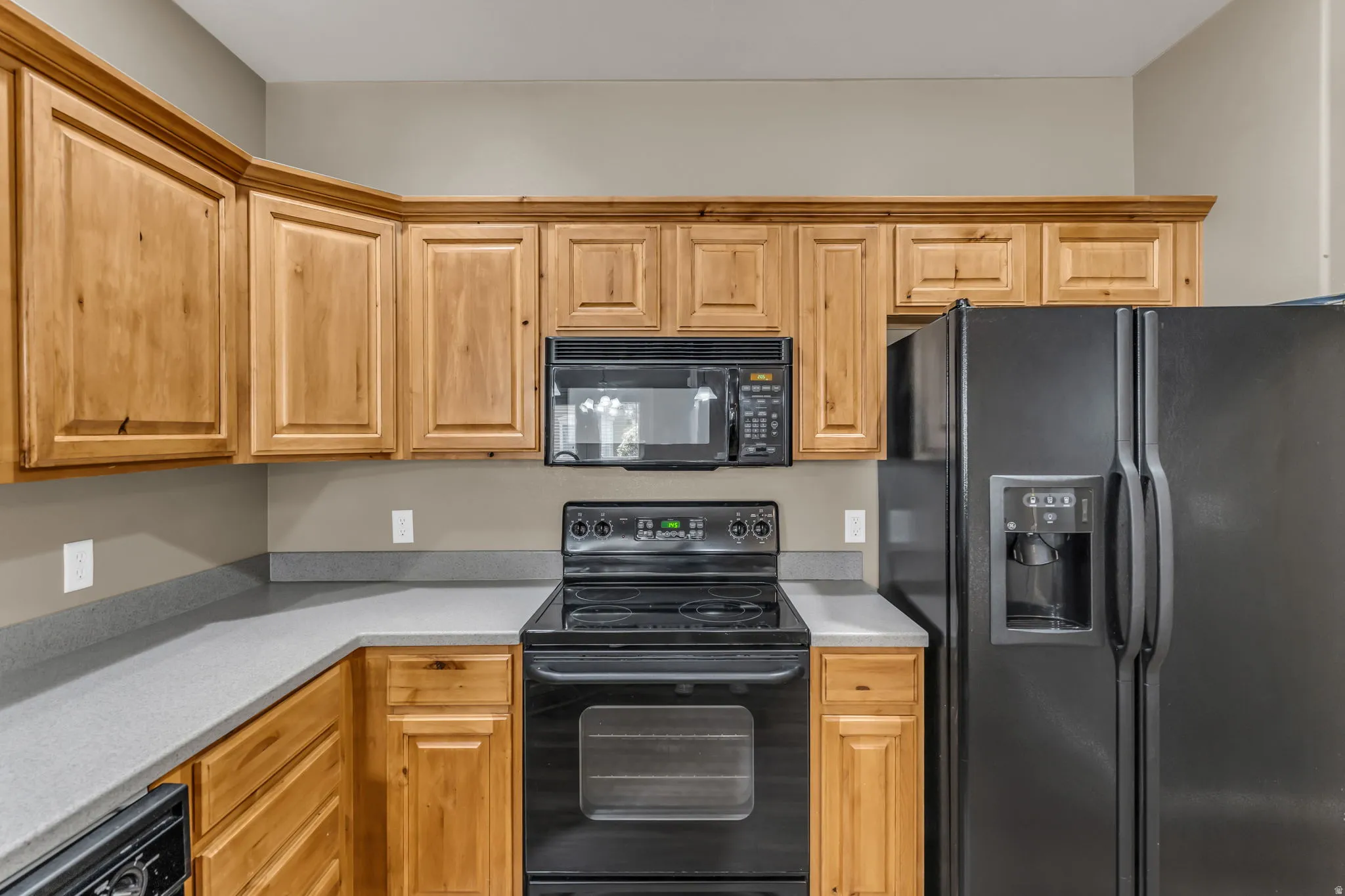 Kitchen featuring wood cabinetry, light gray countertops, black electric range, black microwave, and black side-by-side refrigerator