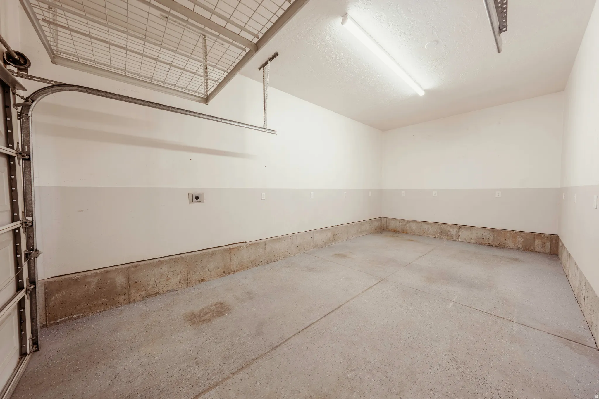Spacious garage featuring a concrete floor, painted walls, overhead fluorescent lighting, and an integrated overhead storage rack system