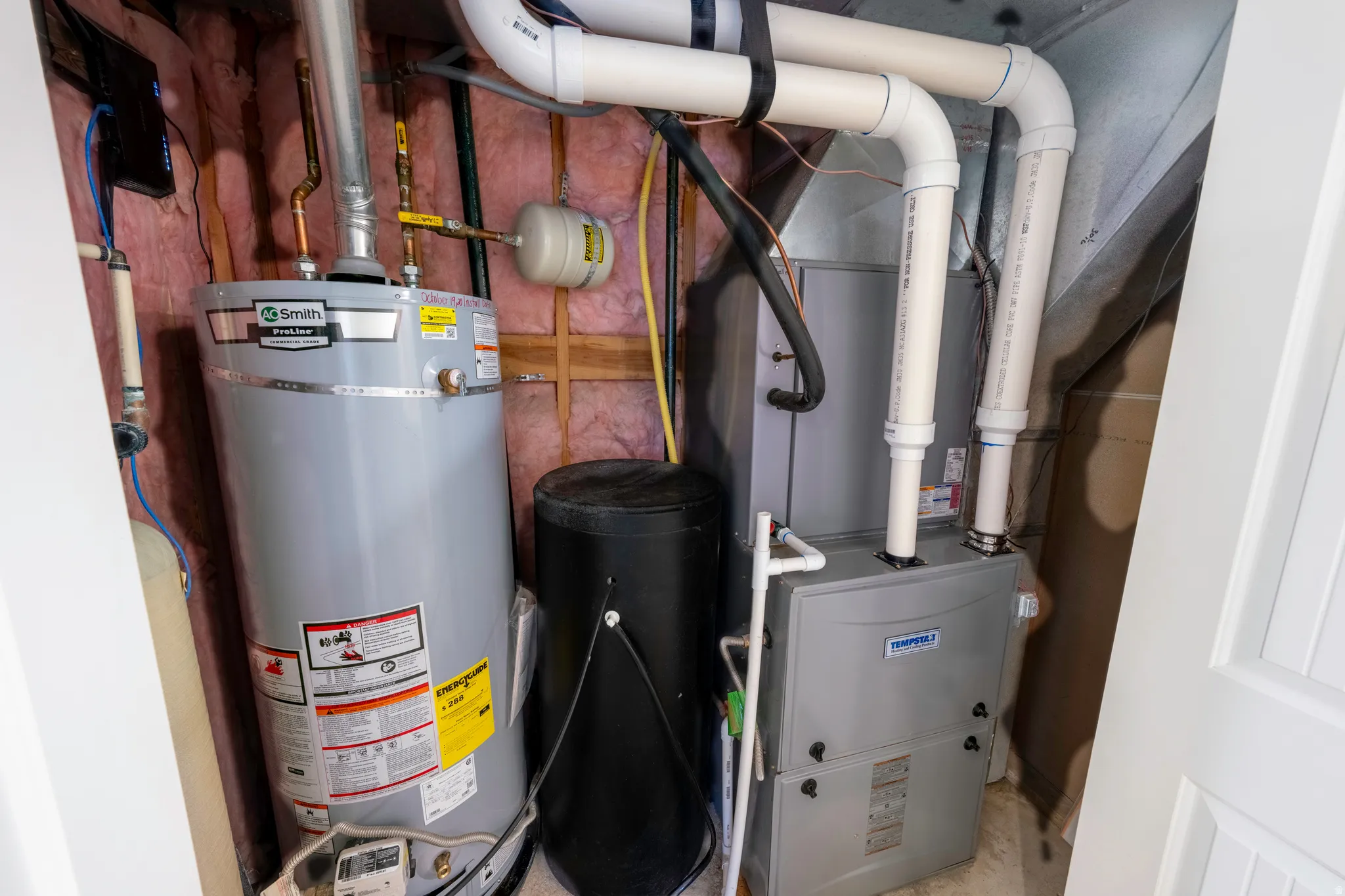 Utility closet featuring a water heater, furnace, air handler, and associated PVC piping