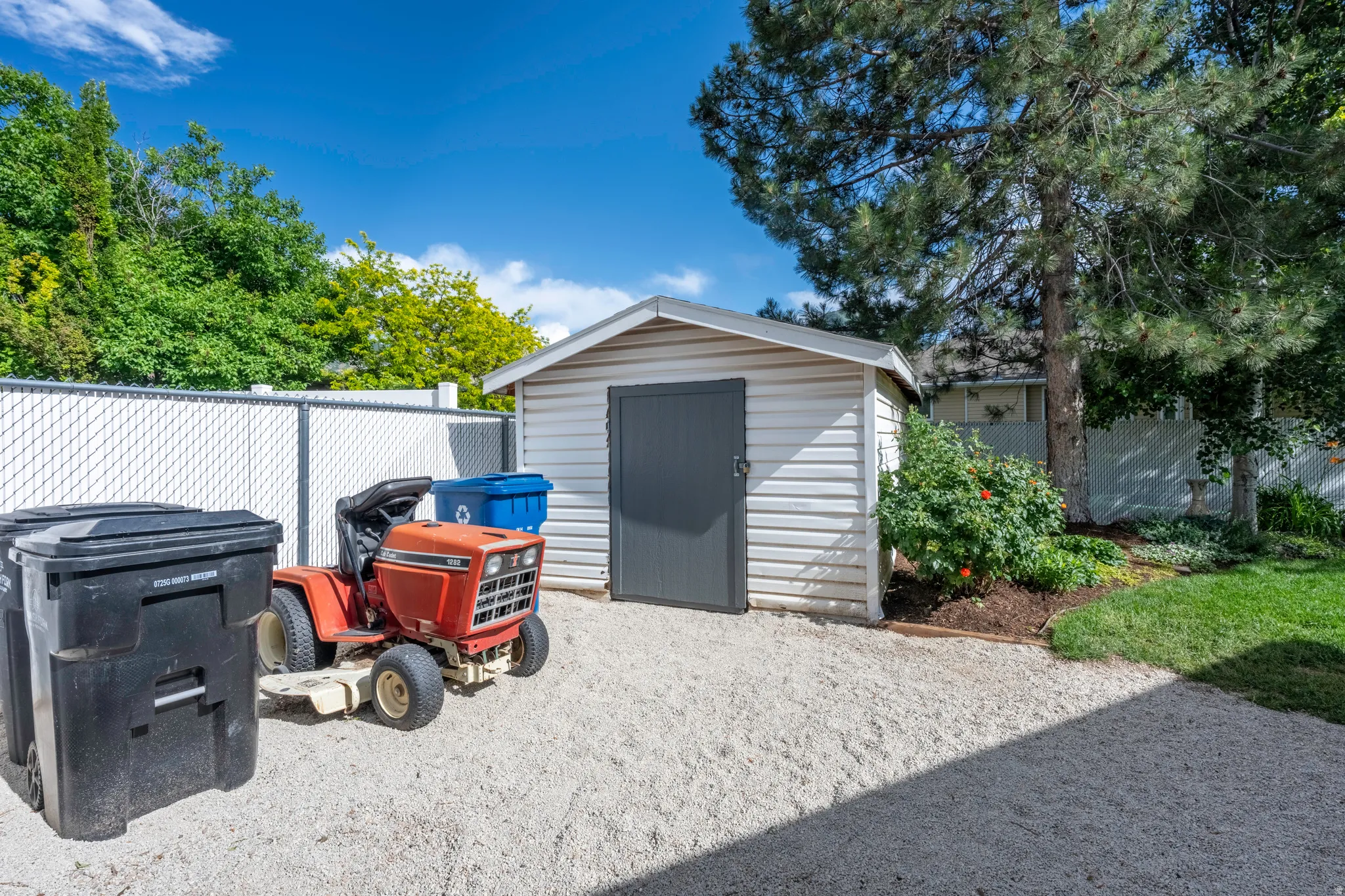 Detached storage shed featuring white siding and a dark gray door, set on a gravel area