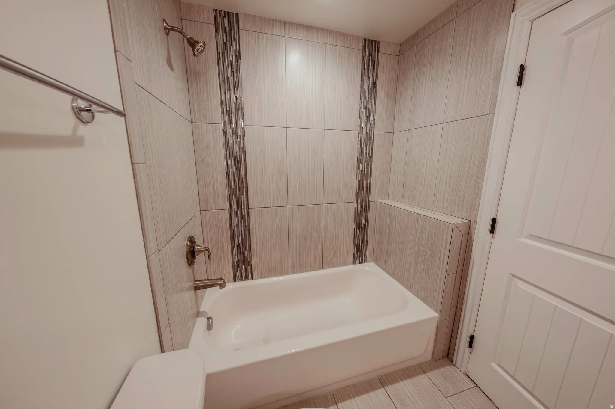 Full bathroom featuring a white porcelain tub, a brushed bronze showerhead and faucet, and floor-to-ceiling tile with decorative accent strips
