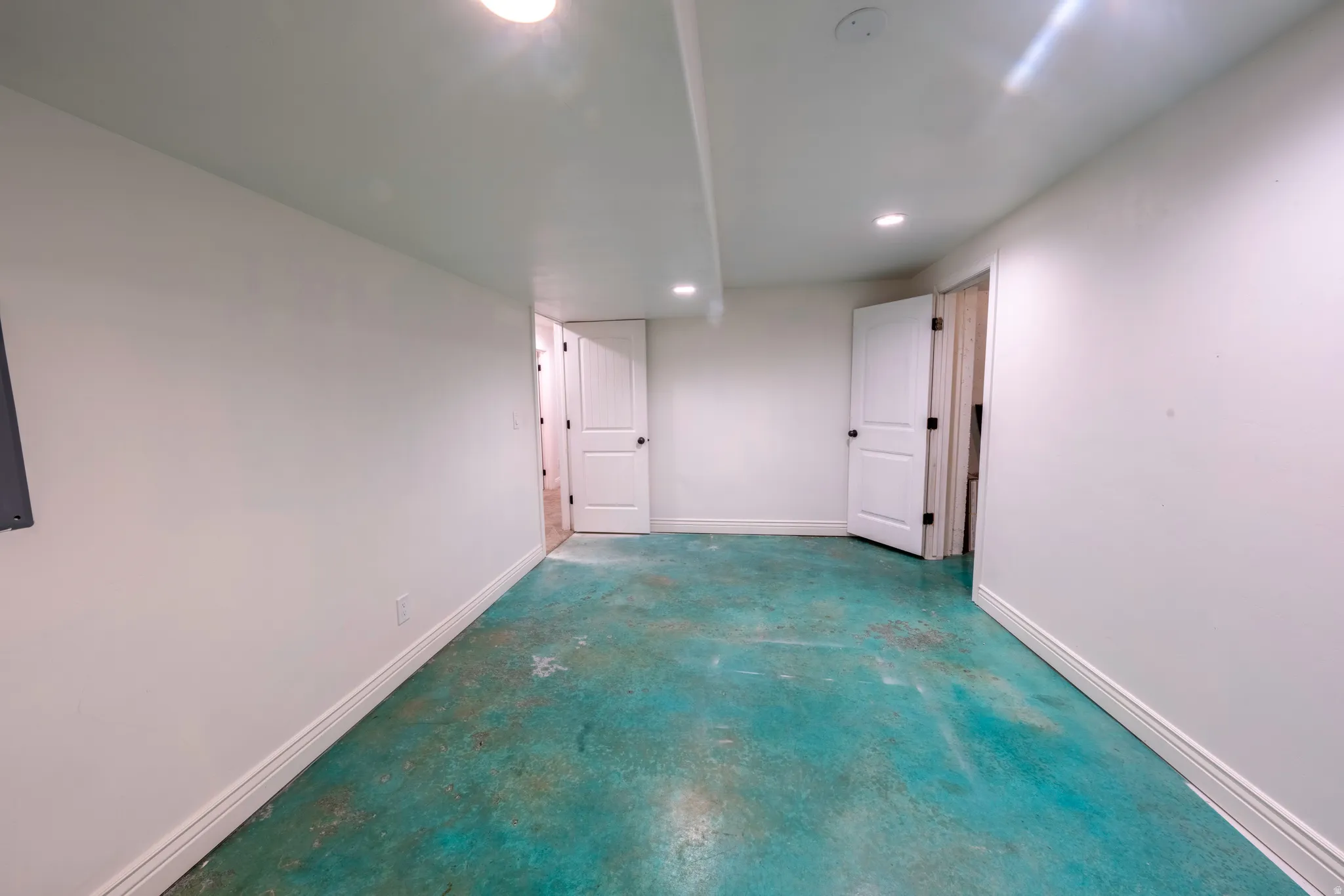 Spacious room with a unique teal-toned concrete floor, crisp white walls, and bright overhead lighting