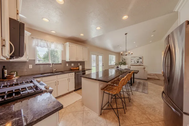 Open concept kitchen featuring recessed lighting, white cabinetry, a dark countertop island with seating, stainless steel appliances, and tile flooring