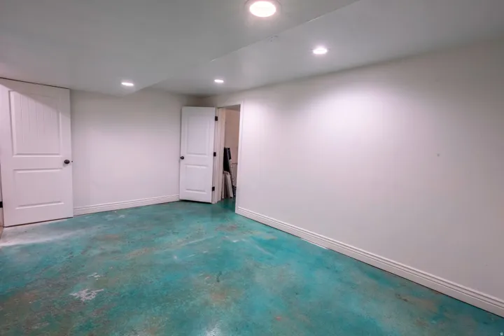 Spacious room featuring white walls, white baseboards, and a turquoise-stained concrete floor