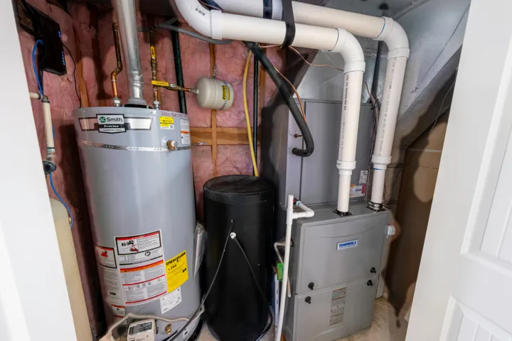 Utility closet featuring a water heater, furnace, air handler, and associated PVC piping
