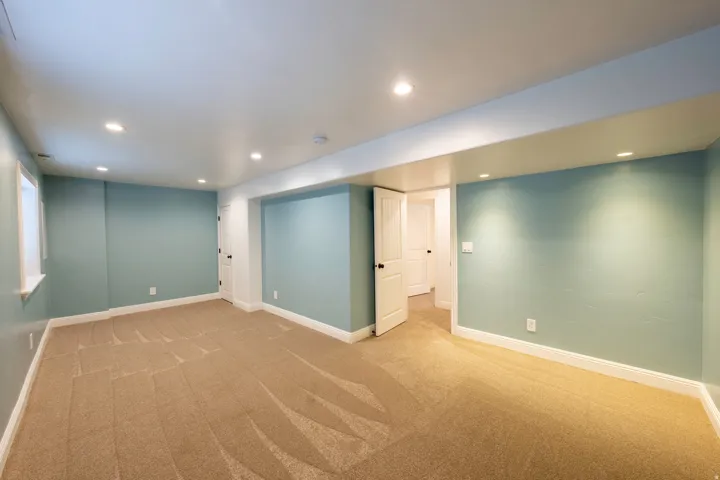 Spacious room featuring neutral carpeting, recessed lighting, light blue walls, white trim, and a white interior door