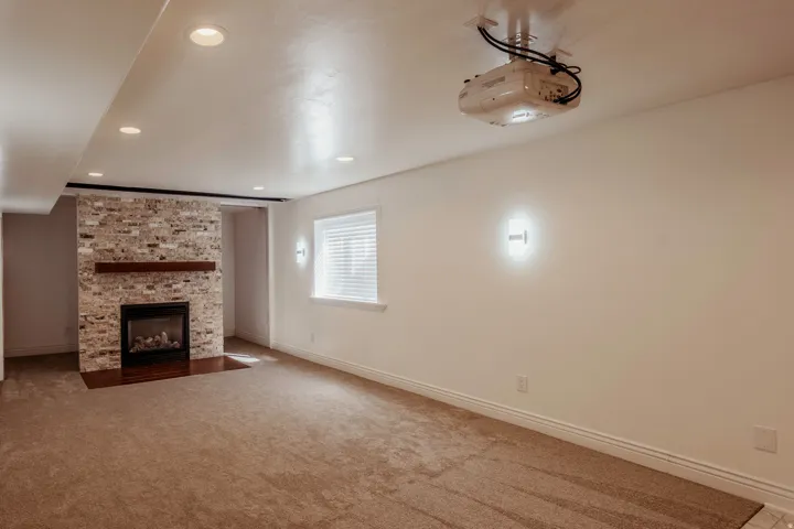 Carpeted room featuring a stone-clad fireplace with a wood mantel, a built-in projector, recessed lighting, and a window with blinds