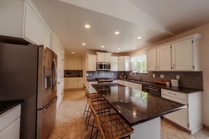 Spacious kitchen featuring an extended island with dark countertops, white cabinetry with crown molding, a stainless steel refrigerator, a built-in microwave, and recessed lighting