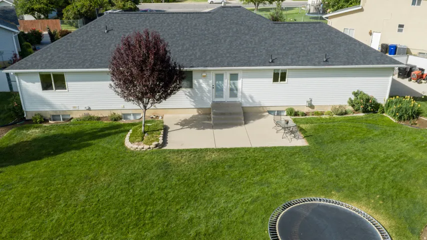 Expansive backyard featuring a lush lawn, concrete patio, and mature landscaping