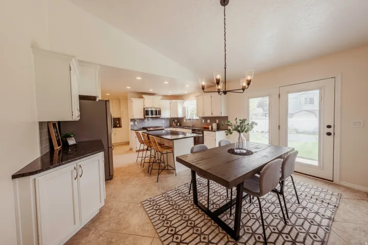 Spacious open-concept kitchen and dining area featuring light-toned tile flooring, white cabinetry, dark countertops, and stainless steel appliances