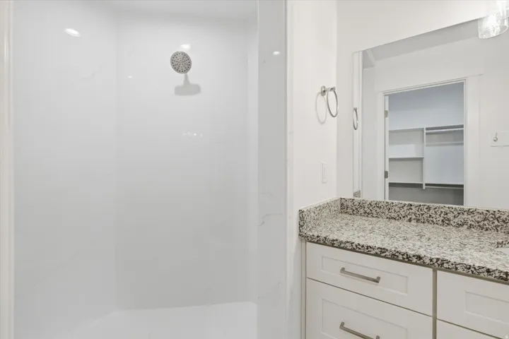 Shower with a rainfall showerhead and white surround, complemented by a vanity featuring a speckled countertop and white cabinetry with brushed nickel hardware