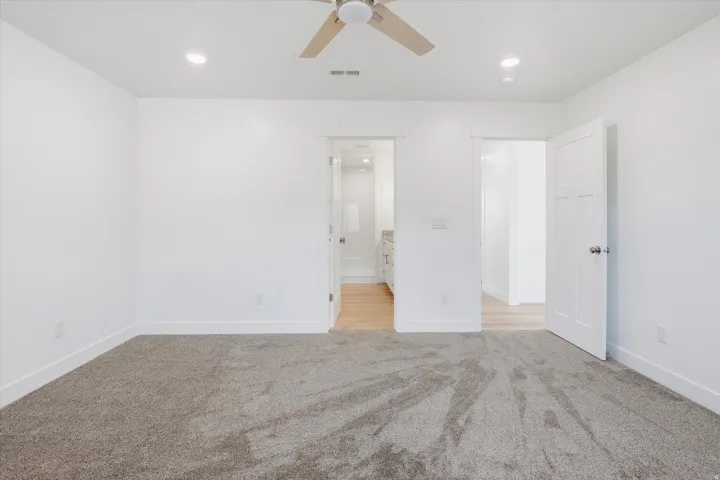 Spacious room featuring neutral carpeting, white walls, recessed lighting, and a ceiling fan with wood-finish blades