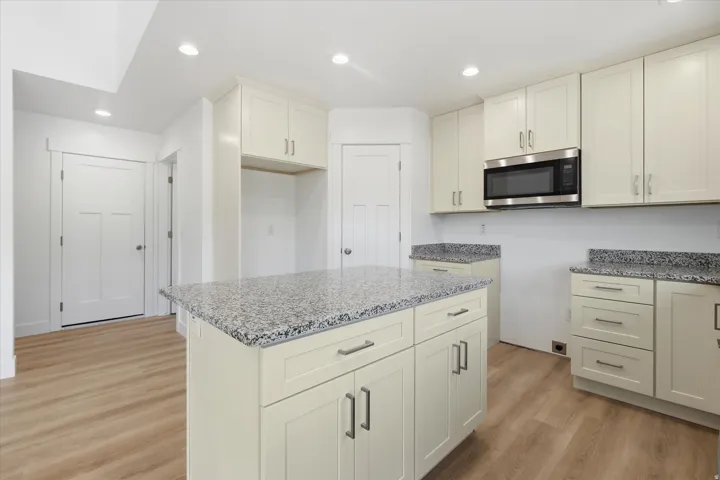 Modern kitchen featuring an island with a speckled countertop, extensive cabinetry, wood-finish flooring, recessed lighting, and a stainless steel microwave
