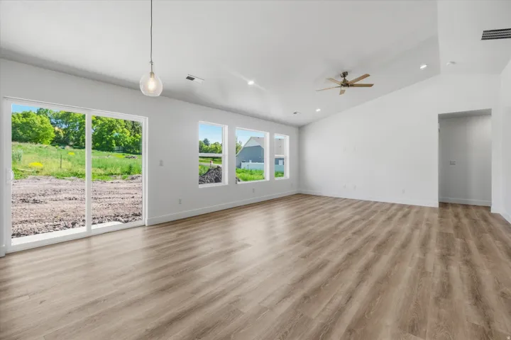 Spacious room featuring wood-finish flooring, white walls, and a vaulted ceiling