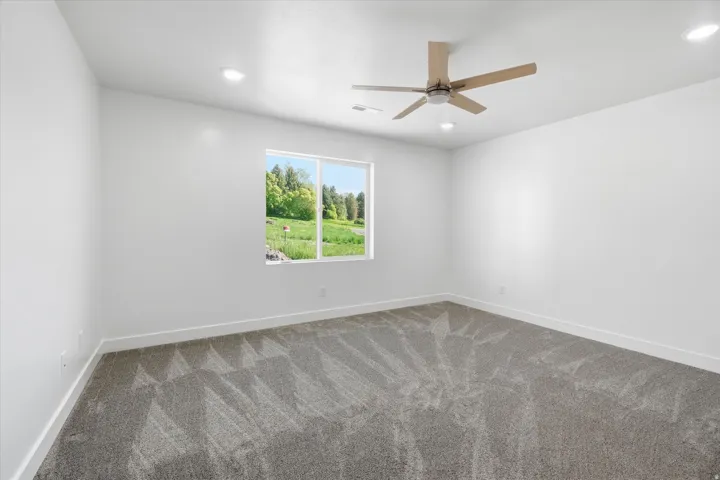Spacious room featuring neutral carpeting, a large window, a wood-finish ceiling fan, recessed lighting, and white baseboards