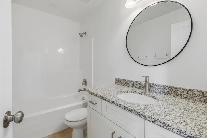 Bright bathroom featuring a white vanity with shaker-style cabinetry, a speckled countertop, an undermount sink with a brushed nickel faucet, a large oval mirror with a black frame, and a white bathtub with a built-in shower