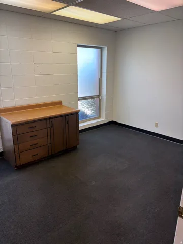 Spacious room featuring block walls, a large window, dark carpet flooring, and a built-in cabinetry unit
