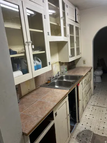 Kitchen featuring a double basin stainless steel sink, tiled countertops, and white cabinetry