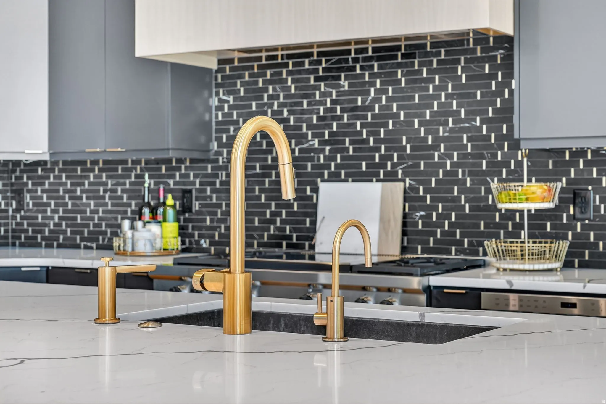 Kitchen featuring a white countertop, gold-finish faucet, black subway tile backsplash, and light gray cabinetry