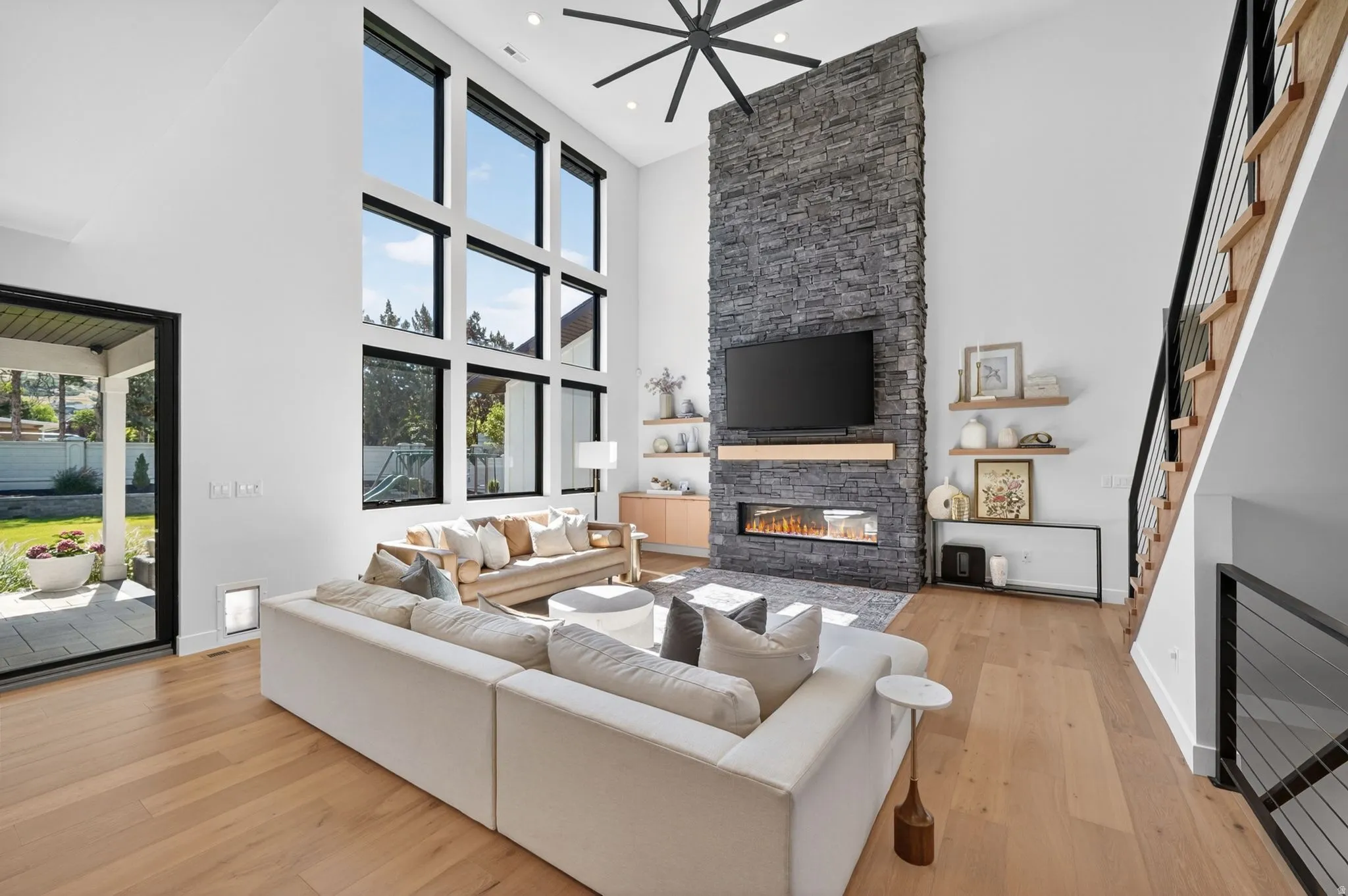 Vaulted ceiling living area featuring a stacked stone fireplace with a linear insert, light wood-finish flooring, and a large grid of windows providing natural illumination