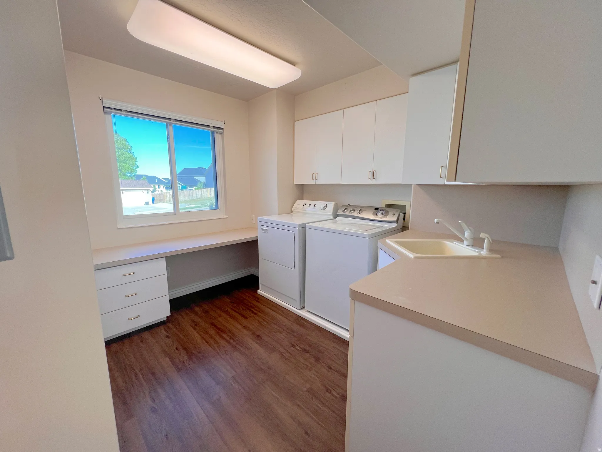 Dedicated utility room featuring wood-finish flooring, white cabinetry, a built-in desk with drawers, an integrated sink, and an overhead fluorescent light fixture