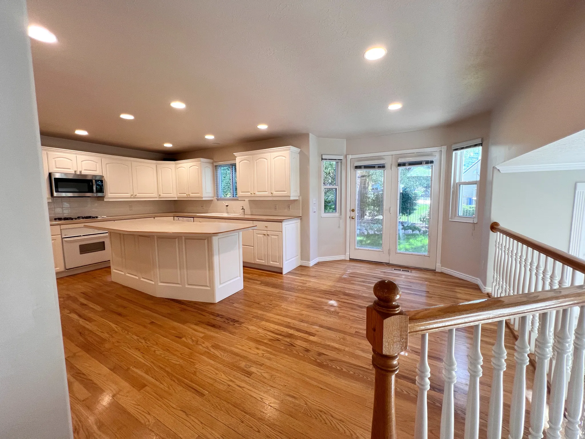 Spacious kitchen featuring white cabinetry, a large island with a light-toned countertop, stainless steel appliances, and wood-finish flooring