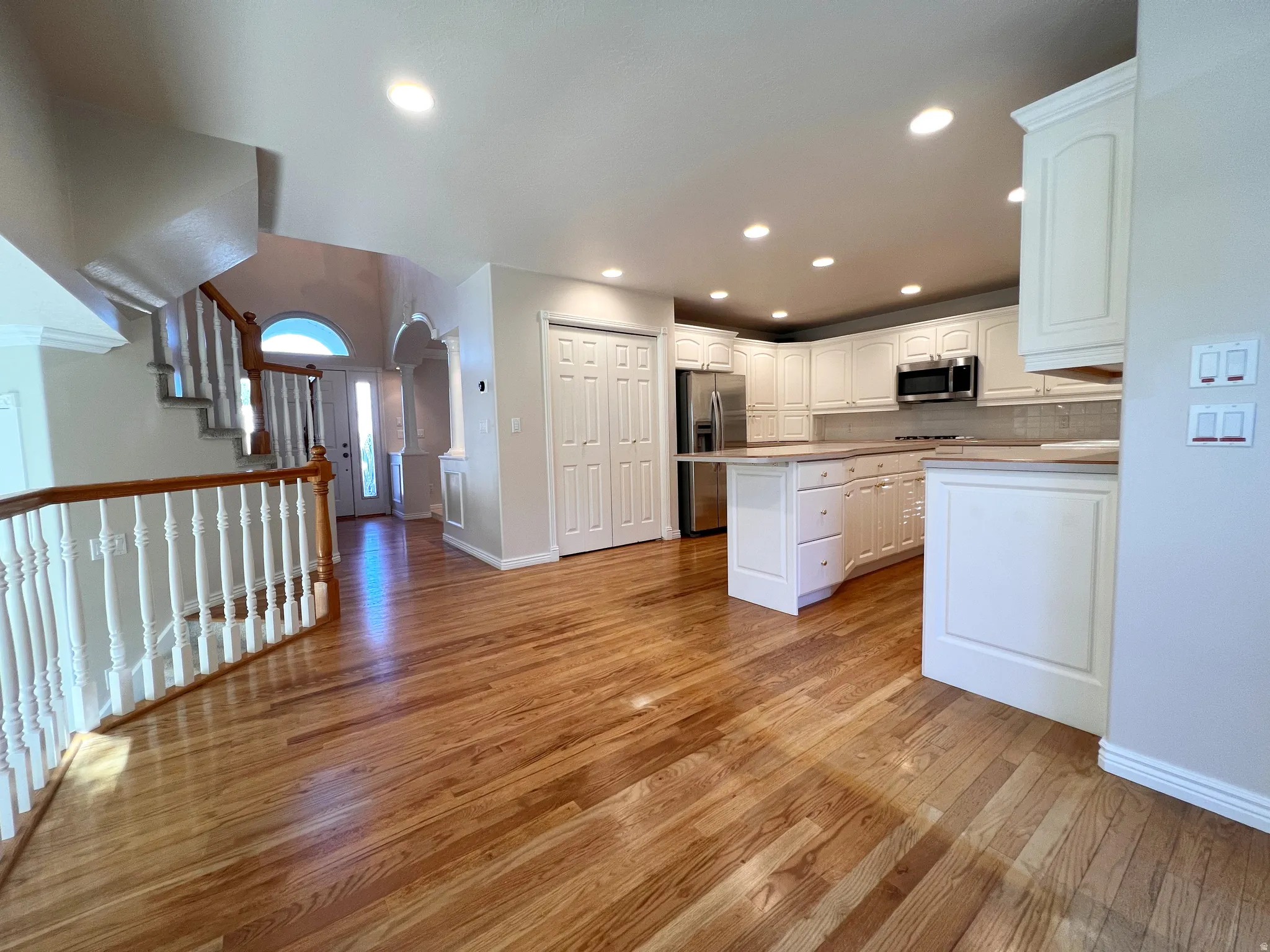 Spacious open-concept kitchen and living area featuring wood-finish flooring, white cabinetry, recessed lighting, stainless steel appliances, and a central kitchen island