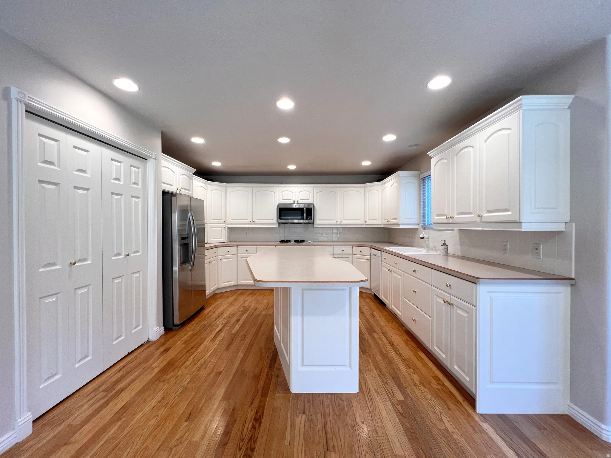 Kitchen featuring extensive white cabinetry, a central island with countertop, wood-finish flooring, a stainless steel refrigerator, and recessed lighting