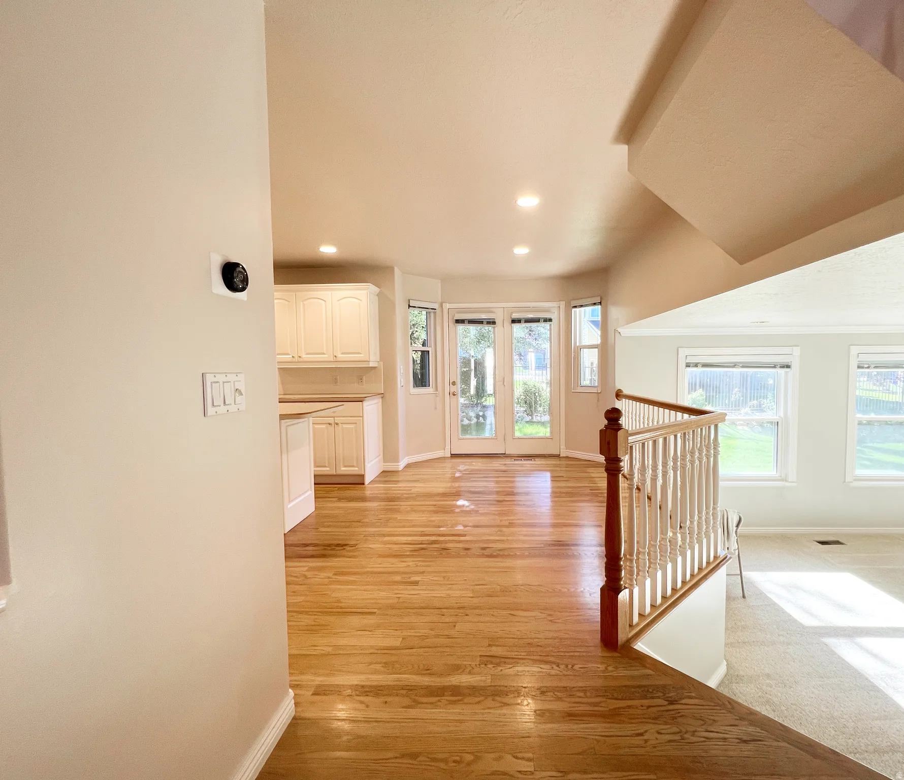 Open-concept living space with wood-finish flooring, white cabinetry, recessed lighting, and a staircase featuring a wood newel post and balusters