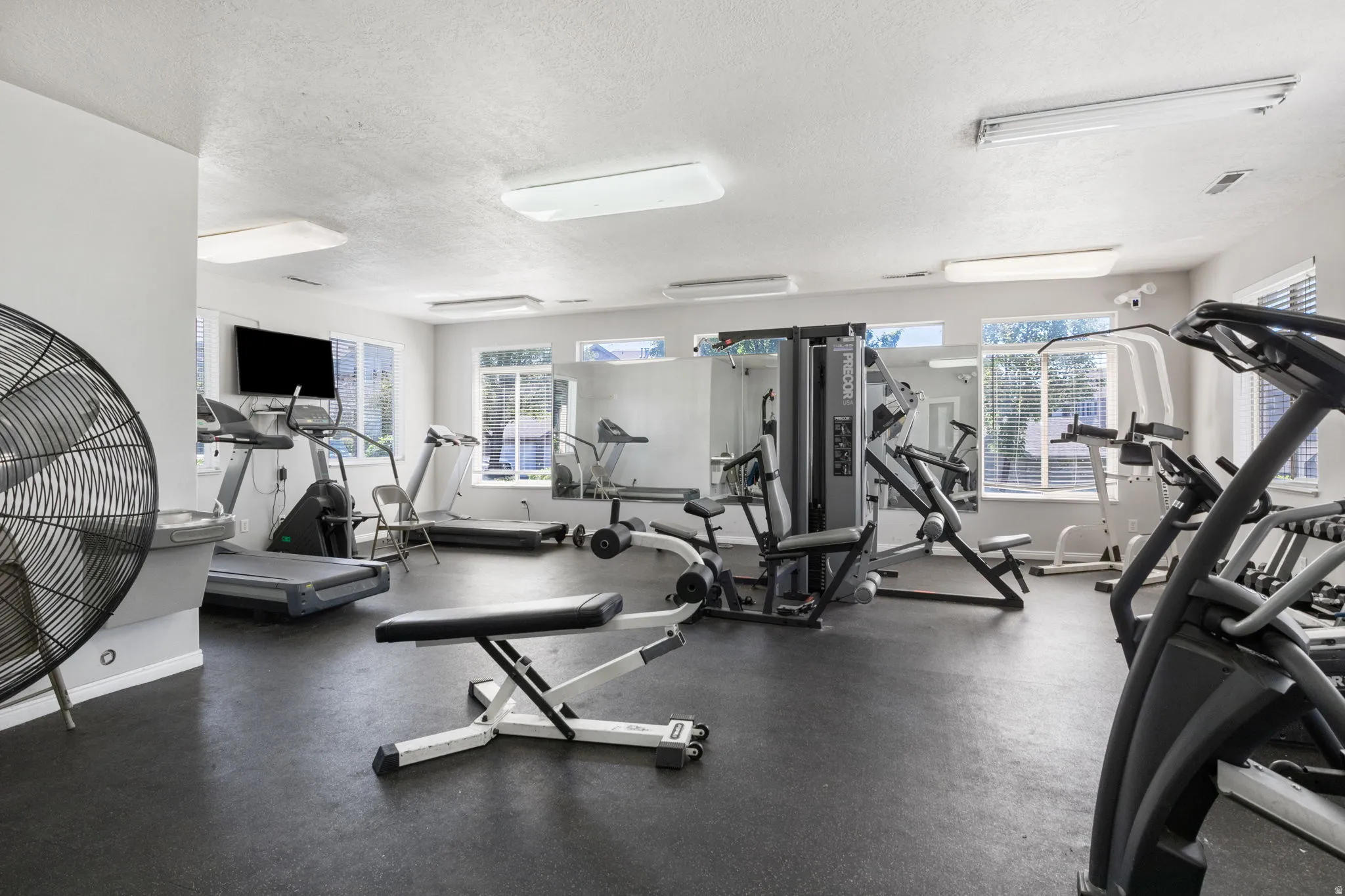 Fitness room featuring extensive exercise equipment, rubber flooring, mirrored walls, and multiple windows with horizontal blinds